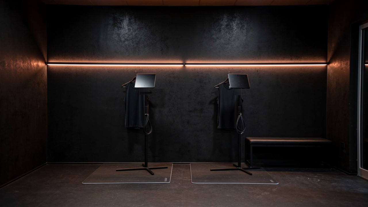 Two training stations on their own mats in a room held for nothing else: a copper light line across the full wall, both side walls in view, a bench at the side
